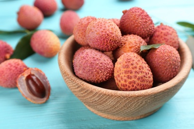Photo of Fresh ripe lychee fruits in bowl on light blue wooden table, closeup