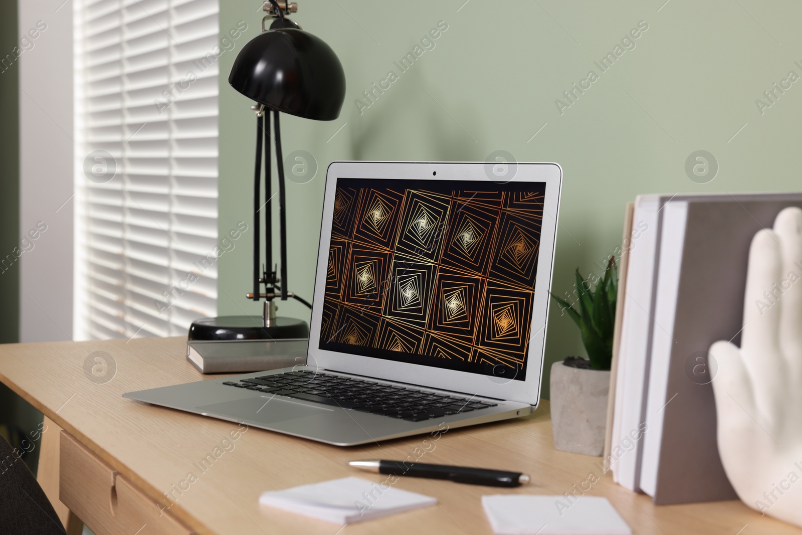 Photo of Modern laptop, books, lamp and stationery on wooden desk near green wall. Home office