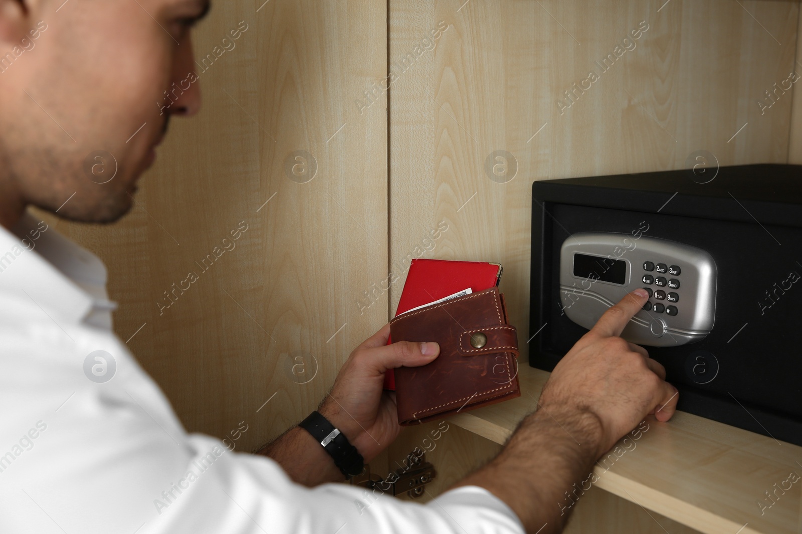 Photo of Man opening black steel safe with electronic lock at hotel, closeup