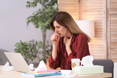 Photo of Sad woman suffering from cold while working with laptop at table