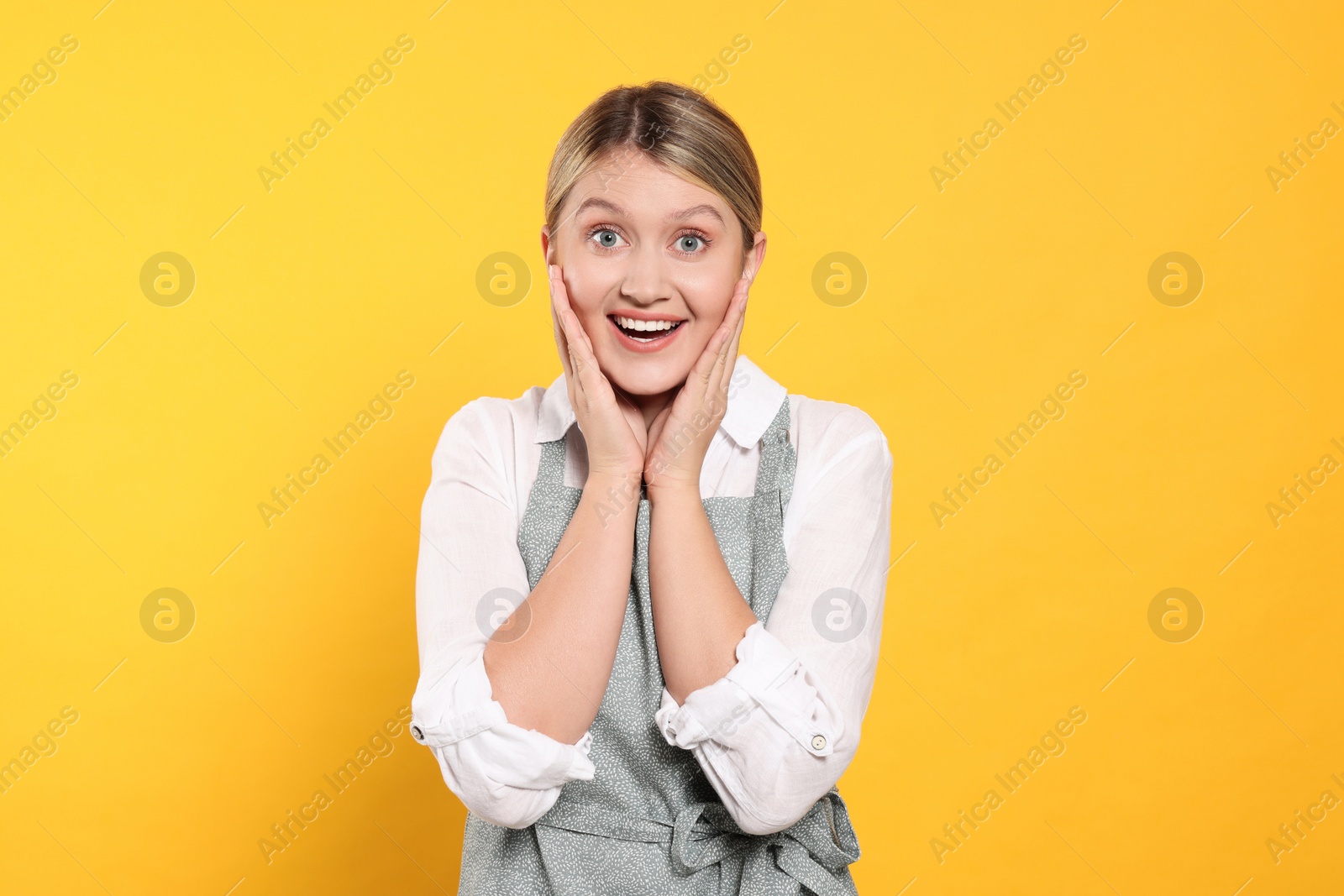 Photo of Beautiful young woman in clean apron with pattern on orange background