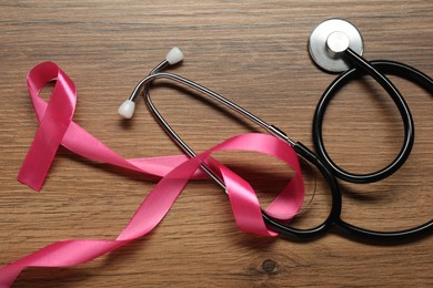 Pink ribbon and stethoscope on wooden table, flat lay. Breast cancer awareness