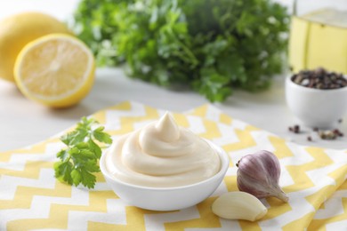 Photo of Tasty mayonnaise sauce in bowl, parsley and garlic on table, closeup