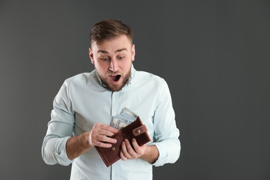 Photo of Emotional young man with wallet full of money on grey background. Space for text