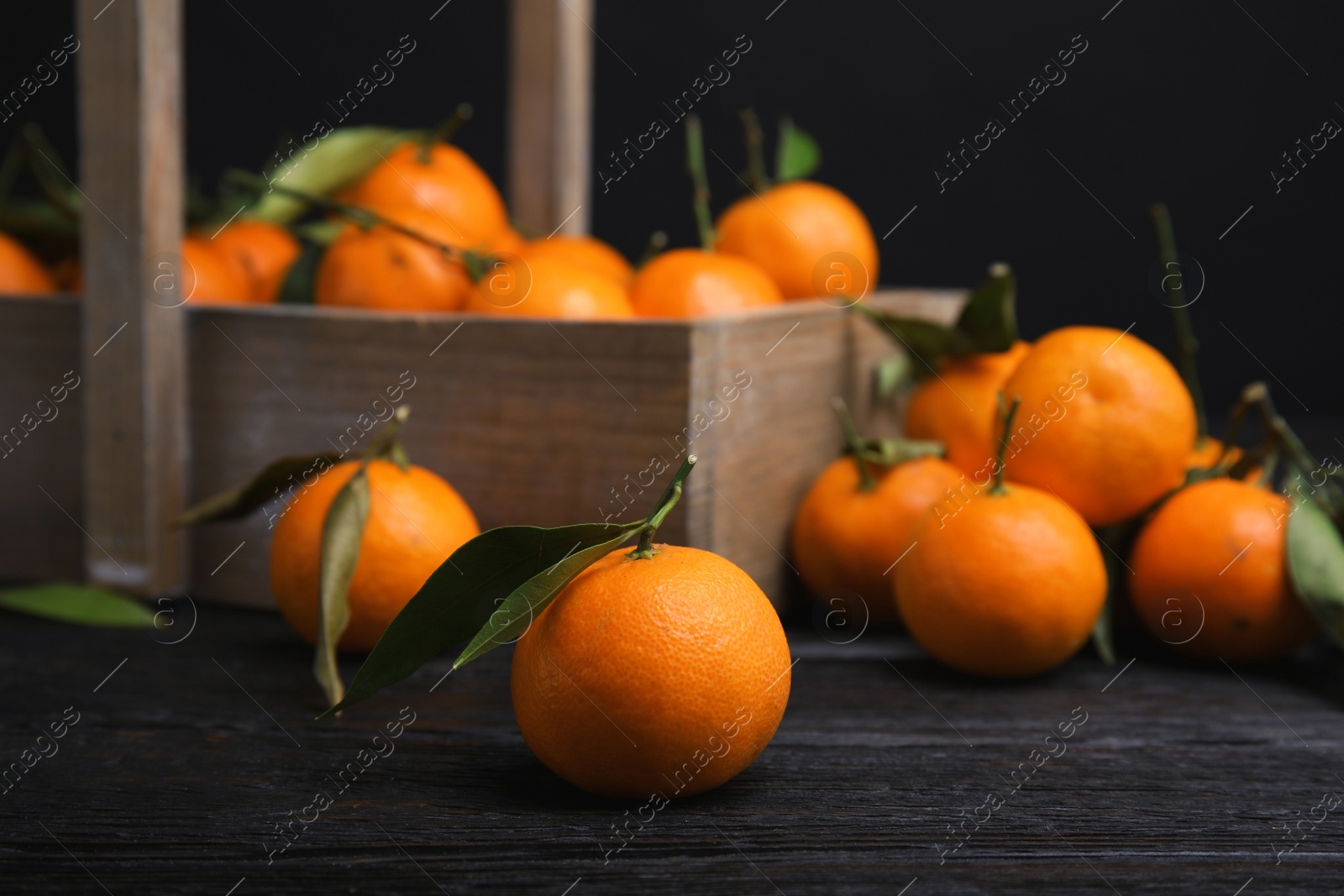 Photo of Fresh ripe tangerines with green leaves and wooden basket on table