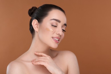 Photo of Woman with swatch of foundation on face against brown background. Space for text
