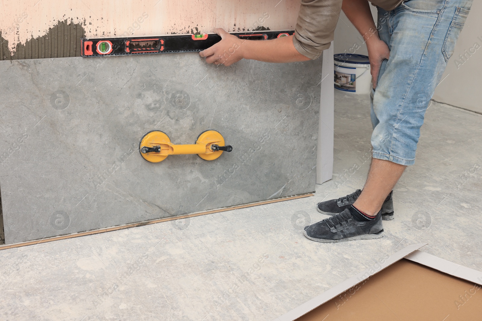 Photo of Professional worker installing tile on wall indoors, closeup