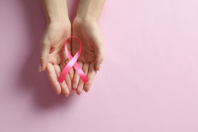 Woman holding pink ribbon on color background, top view with space for text. Breast cancer awareness