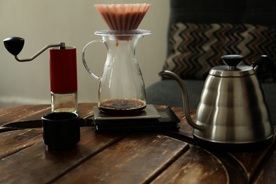 Manual coffee grinder, glass jug with wave dripper and kettle on wooden table in cafe