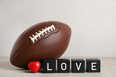 Photo of American football ball, cubes with word Love and heart on light grey table against white background