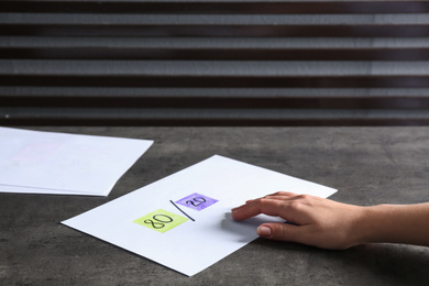 Woman taking paper sheet with 80/20 rule representation at grey table, closeup. Pareto principle concept