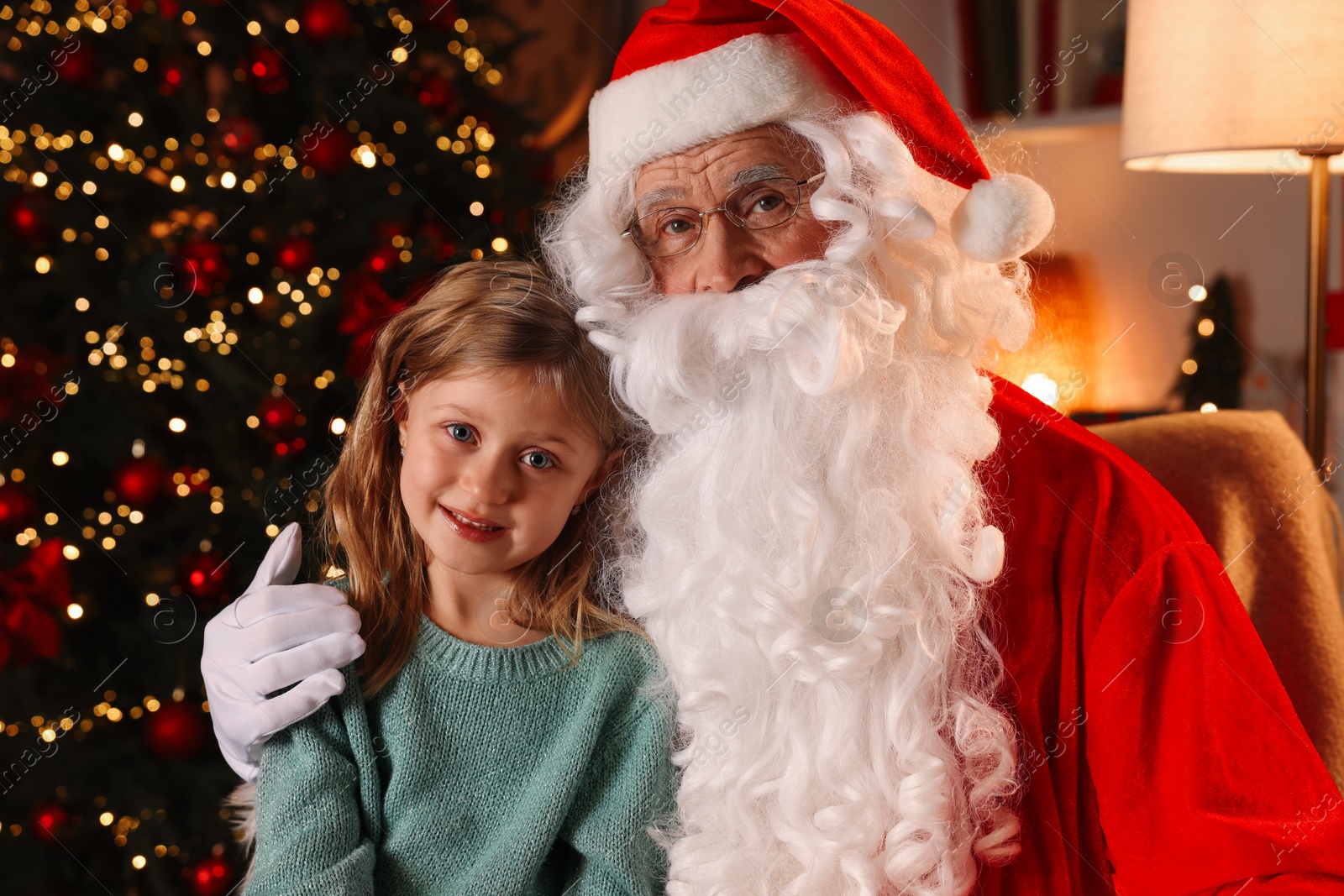 Photo of Santa Claus and smiling little girl in room with Christmas tree