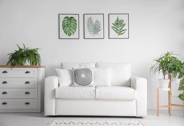 Photo of Beautiful paintings of tropical leaves over sofa in living room interior