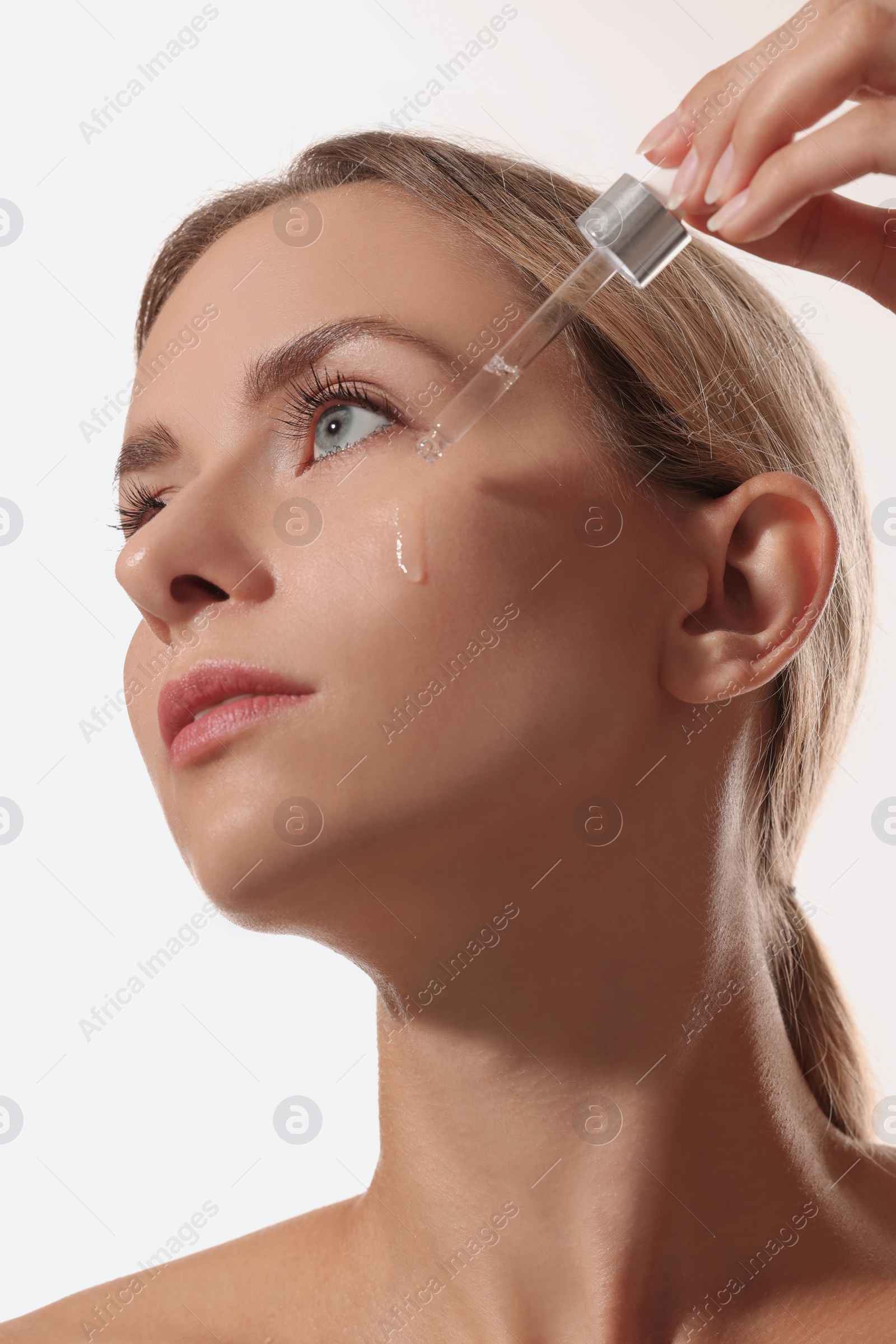 Photo of Beautiful woman applying cosmetic serum onto her face on white background