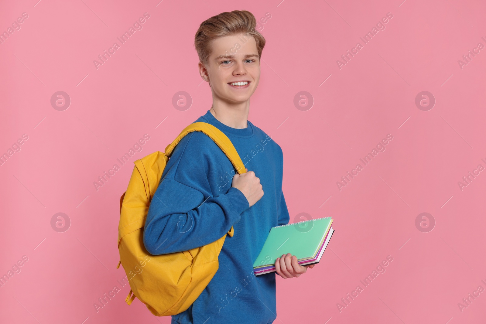 Photo of Teenage boy with books and backpack on pink background