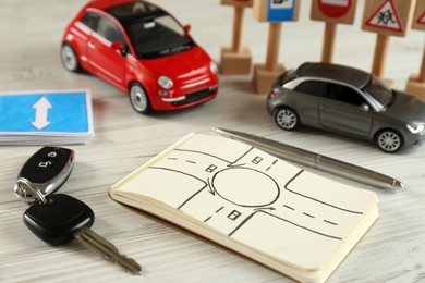 Photo of Composition with workbook for driving lessons and toy cars on white wooden background. Passing license exam