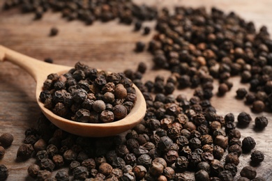 Spoon and black peppercorns on table, closeup