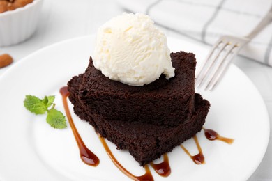 Tasty brownies served with ice cream and caramel sauce on white table, closeup