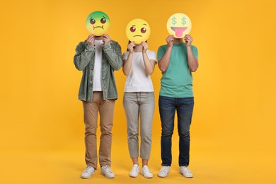 People covering faces with emoticons on yellow background