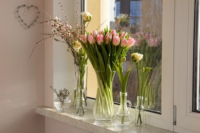 Photo of Many different spring flowers and branches with leaves on windowsill indoors