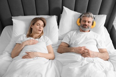 Photo of Smiling man with headphones lying near his snoring wife in bed at home