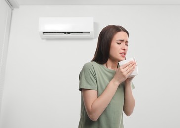 Image of Woman suffering from cold in room with air conditioner on white wall