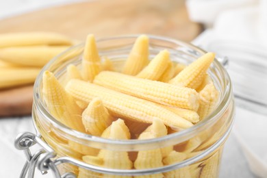 Photo of Jar of pickled baby corn on white table, closeup