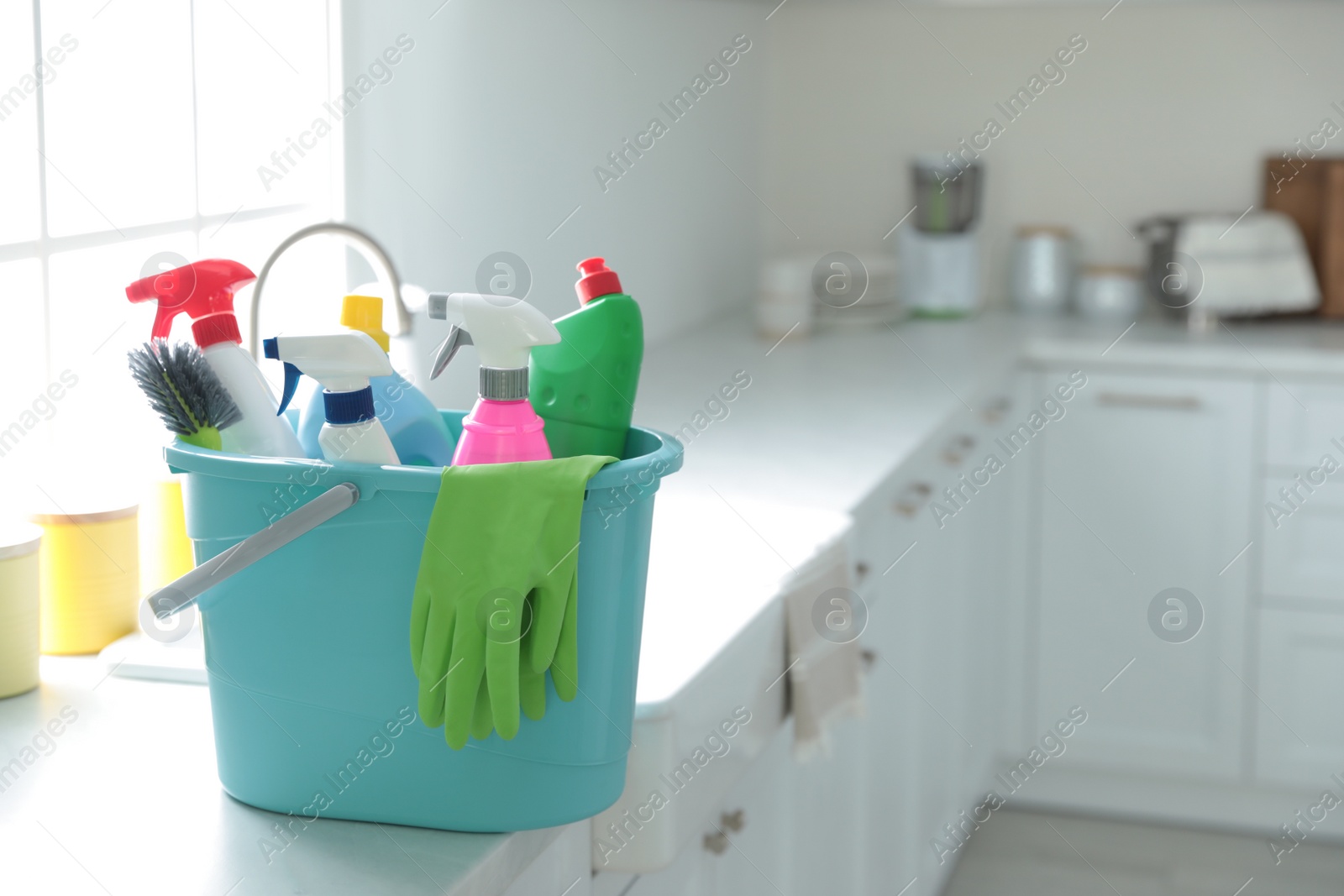 Photo of Plastic bucket with different cleaning supplies on countertop in kitchen. Space for text