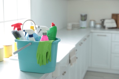 Plastic bucket with different cleaning supplies on countertop in kitchen. Space for text