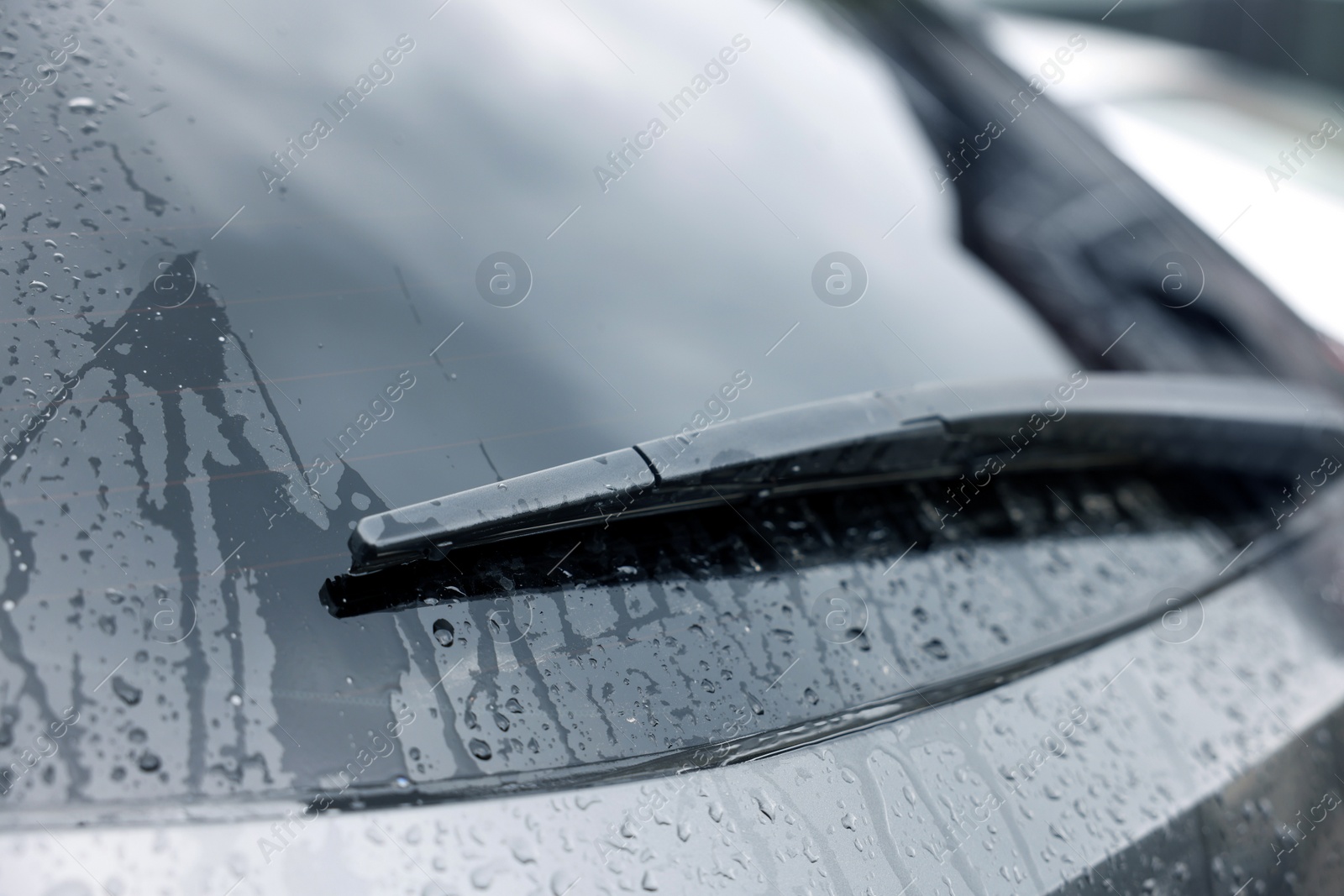 Photo of Car wiper cleaning water drops from rear windshield glass, closeup