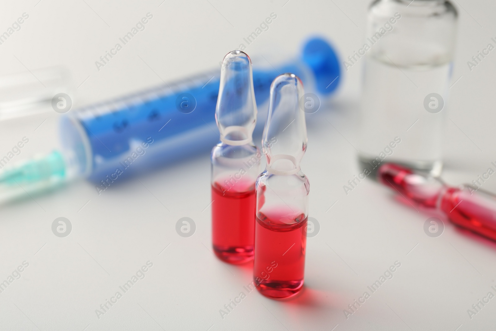 Photo of Glass ampoules with liquid and syringe on white background, closeup