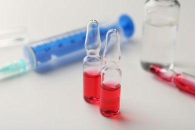 Glass ampoules with liquid and syringe on white background, closeup