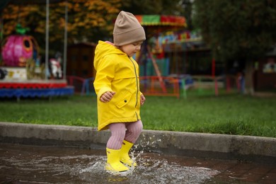 Photo of Cute little girl walking in puddle outdoors