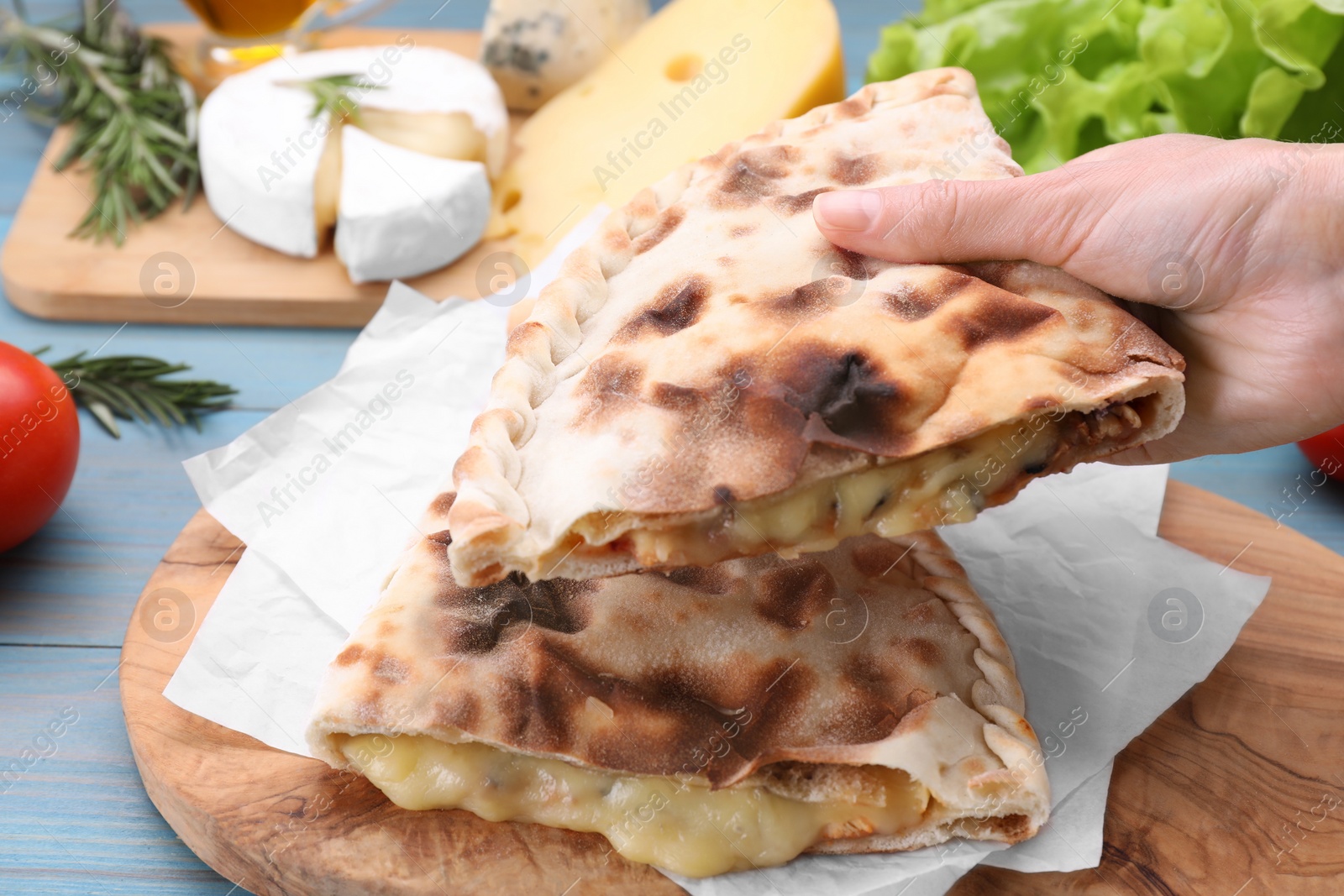 Photo of Woman holding tasty pizza calzone with cheese at light blue wooden table, closeup
