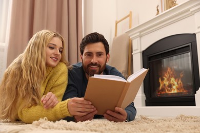 Photo of Lovely couple reading book near fireplace at home