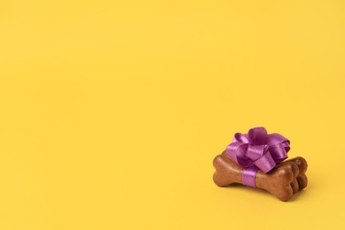 Photo of Bone shaped dog cookies with purple bow on yellow background, space for text