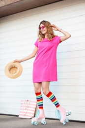 Happy young woman with retro roller skates near white garage door