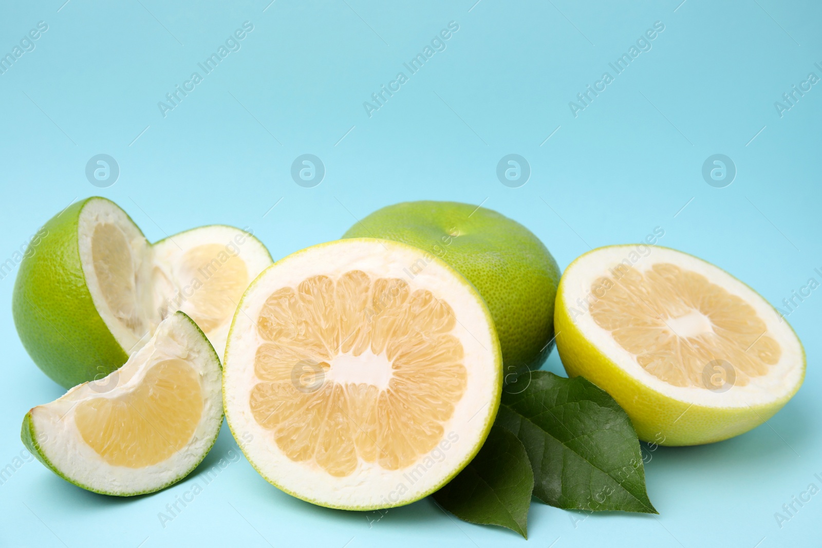 Photo of Whole and cut sweetie fruits with green leaves on light blue background