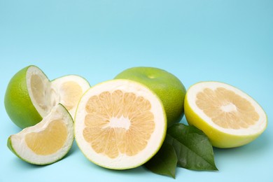 Photo of Whole and cut sweetie fruits with green leaves on light blue background