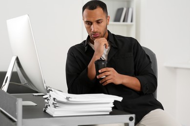 Photo of Man drinking coffee while working with documents at table in office