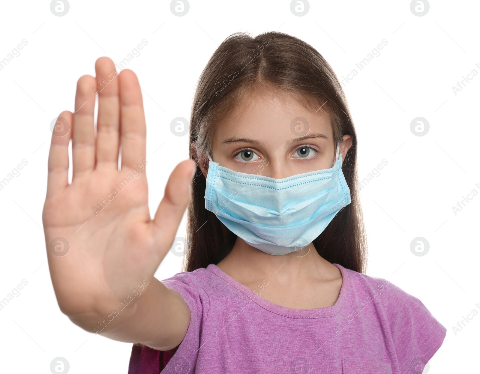 Photo of Little girl in protective mask showing stop gesture on white background. Prevent spreading of coronavirus