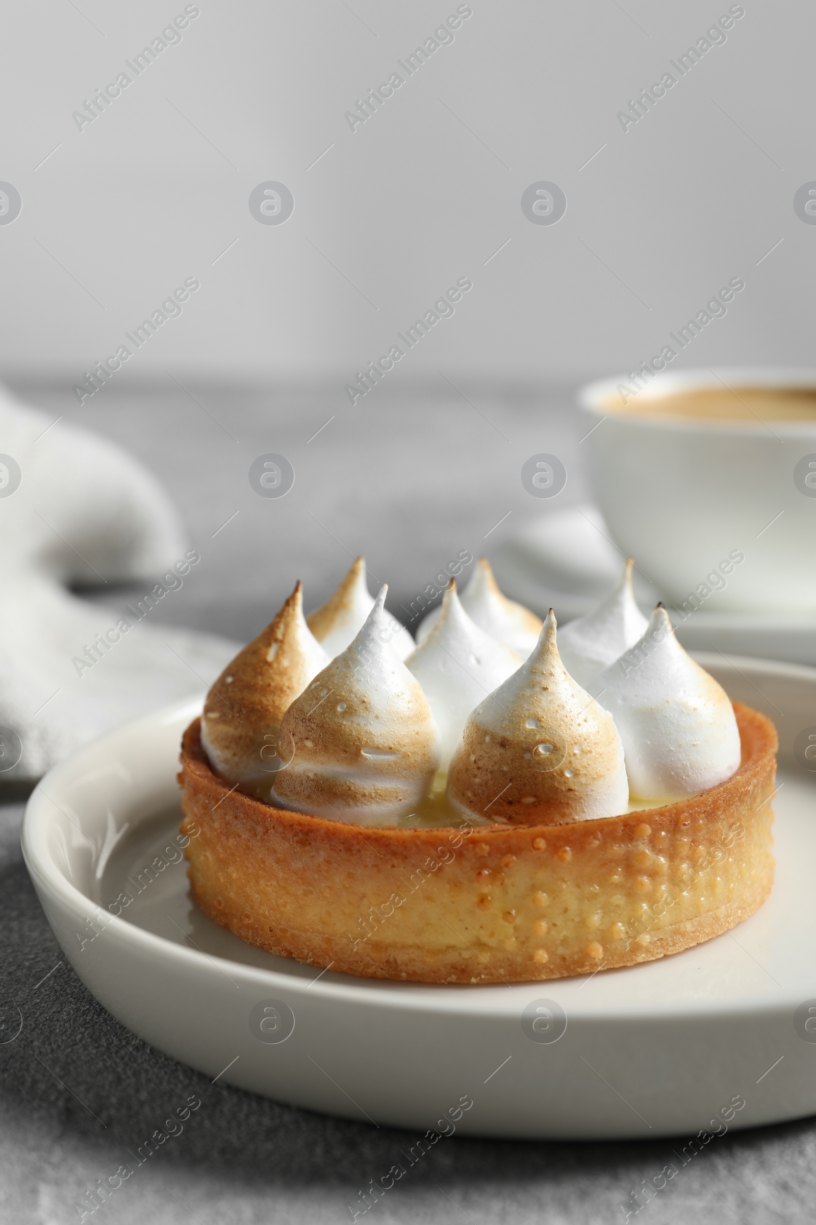 Photo of Tartlet with meringue served on light grey table, closeup. Tasty dessert