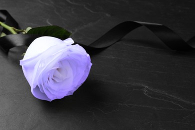 Image of Violet rose with black funeral ribbon on dark table, closeup. Space for text