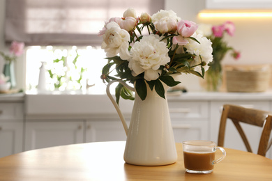 Photo of Beautiful peonies and cup of coffee on wooden table in kitchen. Space for text