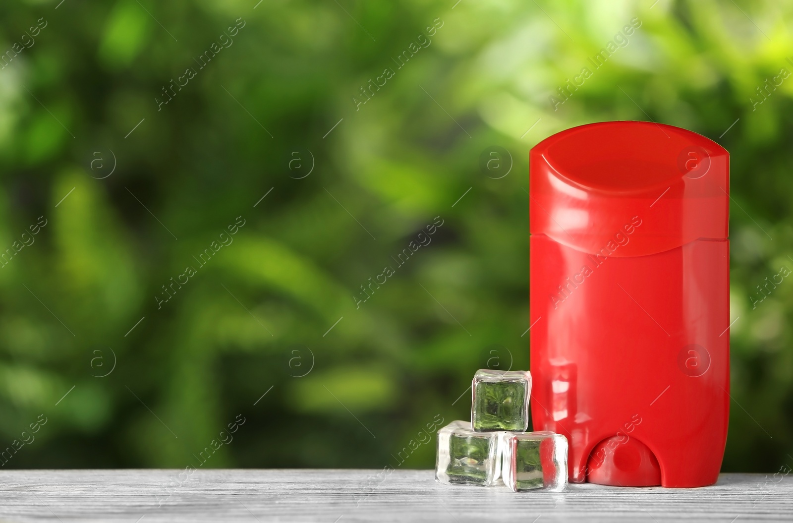 Photo of Natural deodorant with ice cubes on wooden table against blurred green background