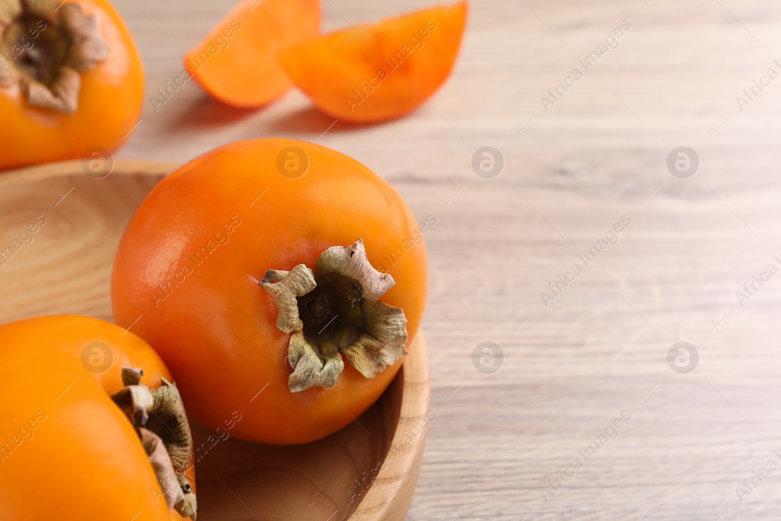 Photo of Delicious ripe persimmons on light wooden table, closeup. Space for text