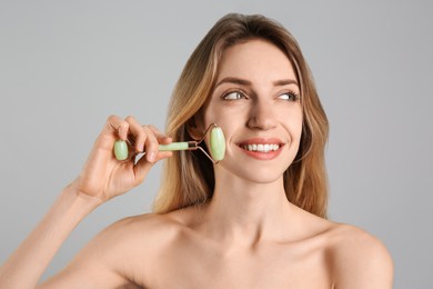 Photo of Young woman using natural jade face roller on light grey background