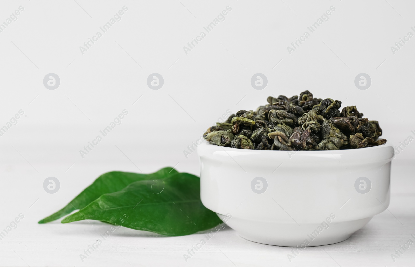 Photo of Dried green tea leaves in bowl on white wooden table, closeup