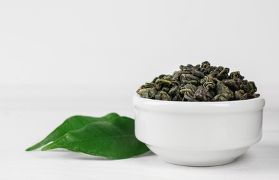 Photo of Dried green tea leaves in bowl on white wooden table, closeup