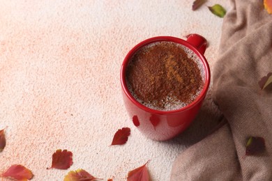 Cup of hot drink, leaves and soft knitted fabric on beige textured table, space for text. Cozy autumn atmosphere